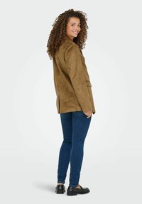 Bruine suède blazer met een kraag, twee voorknoopzakken en een gesplitste achterkant. Gekleed met donkerblauwe skinny jeans en zwarte instappers.