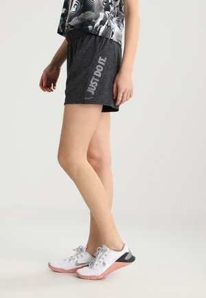 Personne portant un short de sport gris foncé avec le texte « JUST DO IT. » et des baskets blanches avec des semelles roses, se tenant devant un fond clair.