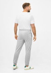Graue Jogginghose mit einem elastischen Bund, kombiniert mit einem weißen T-Shirt und weißen Turnschuhen mit grünen Akzenten, von hinten betrachtet.