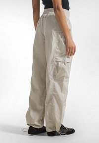 Lyse beige cargobukser med elastisk taljebånd, sidelomme med mesh-detaljer og justerbare manchetter med snore.
