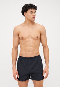 Shorts de bain noirs avec une taille élastique, un détail de bouton à l'avant, et un tissu léger, conçus pour le confort et la liberté de mouvement.