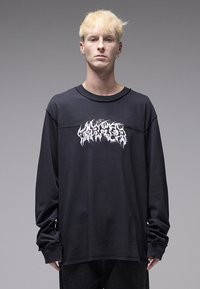 Μαύρο μακρυμάνικο t-shirt από βαμβάκι, με υφασμένο, στιλιζαρισμένο λευκό γραφικό σχέδιο στο μπροστινό μέρος και ελαφρώς φαρδιά εφαρμογή.