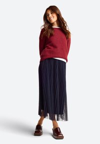 Maroon fluffy sweater layered over a white top, paired with a pleated dark navy skirt and dark brown platform shoes.