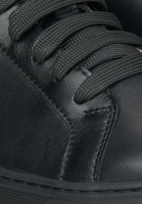 Černé kožené tenisky s texturovaným povrchem, vybavené černými tkanými šňůrkami, prošívanými detaily a gumovou podrážkou.