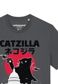Grijze T-shirt met een zwarte katten silhouet met opgestoken poot, rode cirkel achtergrond, "CATZILLA" tekst en illustraties van helikopters en een gebouw.