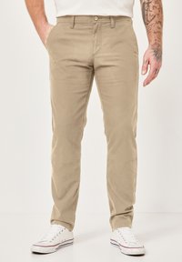 Khaki-Chinos aus Baumwolle mit geradem Bein, Knopf- und Reißverschluss, Fronttaschen und getragen mit weißen Sneakers.