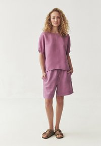 Top in lino lilla con maniche corte a sbuffo e scollatura rotonda, abbinato a pantaloni corti coordinati con cintura elastica e stringente.