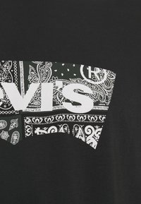 T-shirt noir avec un motif graphique paisley noir et blanc, affichant le texte "LEVI'S" en blanc de manière bien visible. Matière en coton doux.