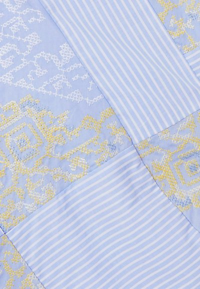 Trapunta azzurro pallido con motivi geometrici gialli e bianchi ricamati in modo alternato e quadrati di tessuto a righe azzurro chiaro e bianco.