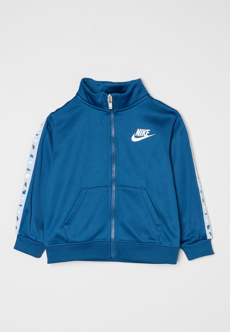 Chaqueta azul con cremallera hecha de tejido suave. Cuenta con un cuello alto, dos bolsillos frontales y el logo blanco de Nike. Detalles a rayas en las mangas.