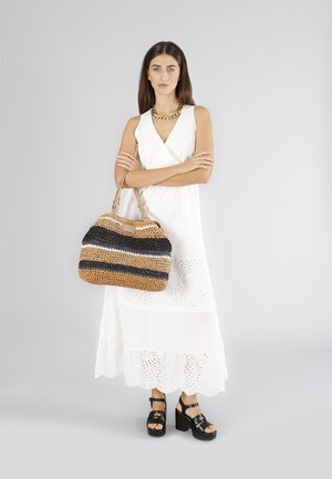 Woven handbag w paski w odcieniach brązu, czerni i bieli, zestawiona z białą sukienką z ażurowymi detalami oraz czarnymi sandałami na koturnie.