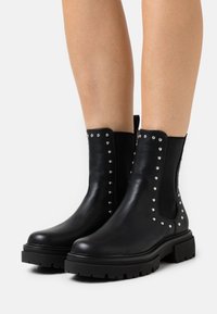 Black leather ankle boots with elastic side panels, silver studs along the edges, and chunky black rubber soles. Smooth texture.