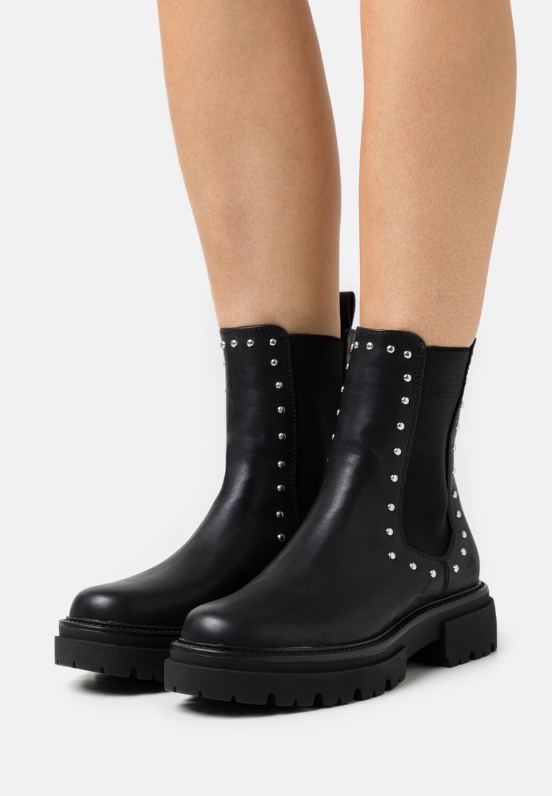 Black leather ankle boots with elastic side panels, silver studs along the edges, and chunky black rubber soles. Smooth texture.