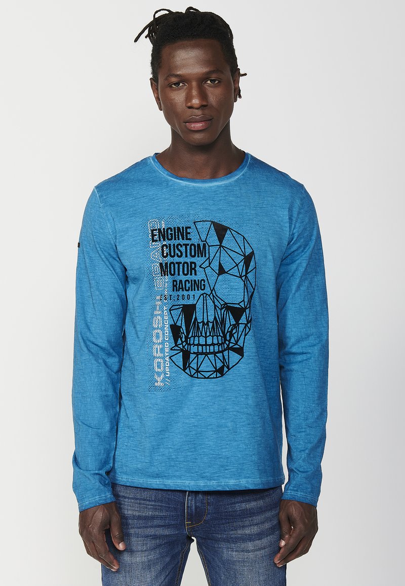 Long-sleeve blue T-shirt made of textured fabric, featuring a black geometric skull graphic and text on the left side.