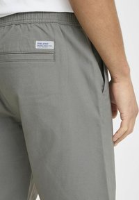 Gray shorts with a textured fabric, featuring a side pocket, elastic waistband, and a patch label on the back.