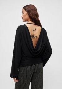 Mustast riidest ülaosa sügava V-kaelusega seljal, õhukeste rihmade ja siledapinnalise tekstuuriga. Kombineeritud vertikaalsete triipudega pükstega.