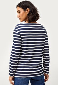 Marineblauwe en witte gestreepte long sleeve top met een bootnek, voorzien van een relaxte pasvorm en zachte stof, gecombineerd met blauwe jeans.