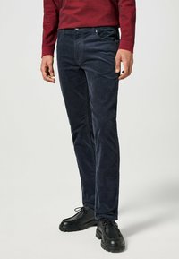 Marineblauwe corduroy broek met een slim fit, vijf zakken en een gladde textuur. Gecombineerd met zwarte veterschoenen.