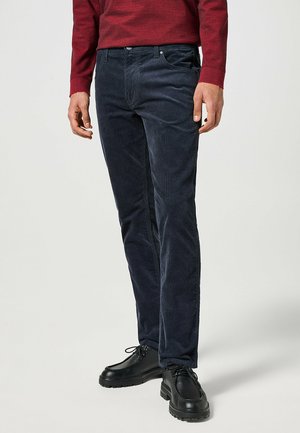 Granatowe spodnie korduroy w slim fit, z pięcioma kieszeniami i gładką fakturą. W połączeniu z czarnymi sznurowanymi butami.