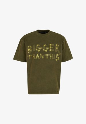 Olive spalvos medvilnė marškinėliai su trumpomis rankovėmis ir apvaliu kaklu. Yra ryškiai geltonas užrašas "DIDESNI NEI ŠIS" žaismingu, nereguliariu šriftu.