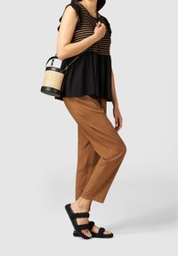 Zwart en bruin gestreepte top met gerimpelde mouwen, bruine tapering broeken en zwarte gevlochten sandalen. Accessoire: cilindervormige geweven handtas.