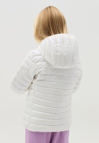 Veste puffer blanche avec capuche, dotée d'un design matelassé et de coutures horizontales, présentant une texture brillante.