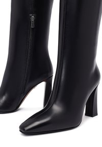 Bottes en cuir noir jusqu'au genou avec un bout pointu, un talon block haut et des détails de fermeture éclair sur le côté. Texture lisse avec un design épuré.