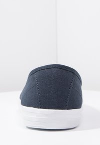 Chaussure slip-on en toile bleu marine, avec une surface texturée, une semelle en caoutchouc blanche et des détails de coutures simples.