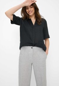 Zwarte linnen shirt met een V-hals en opgerolde mouwen, gecombineerd met lichtgrijze linnen broek met een knoop aan de voorkant en zijzakken.