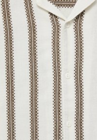 Camisa blanca con patrón de rayas marrones y botones. La textura de la tela parece ligera y tejida, con costuras detalladas a lo largo de las rayas.