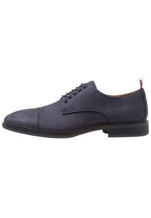 Chaussure Oxford en daim bleu marine à lacets, bout droit, semelle noire et languette rouge au talon, vue de profil.