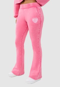 Roze sweatpants gemaakt van zacht materiaal met een uitlopende pasvorm, met een decoratief wit hartlogo op de linker dij en zijzakken.