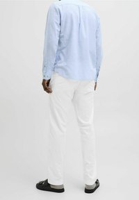 Světle modrá košile s dlouhým rukávem a knoflíkovými manžetami, bílé kalhoty a černé sandály s tlustým páskem. Hladká látka a volný střih.