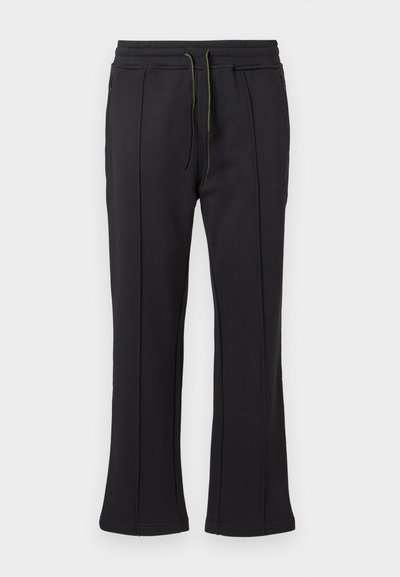 Black sweatpants with a flared leg design, featuring two side zip pockets and adjustable drawstring waistband. Smooth texture and minimal branding.