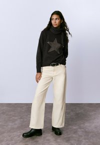Suéter de punto gris oscuro con un patrón de estrellas, combinado con pantalones anchos color crema y botas de tobillo negras. El cinturón tiene tachuelas decorativas.