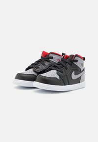 Sneaker in pelle nera e grigia con accenti rossi, punta forata, lacci neri e suola in gomma bianca. Presenta il logo iconico sul lato.