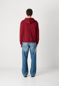 Red hoodie with a drawstring hood, paired with light blue, wide-leg jeans. Smooth fabric texture and distinct stitching on the jeans.
