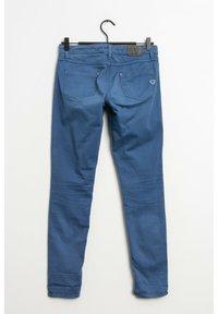 Modré džíny skinny visící na háčku, s malým srdíčkovým logem na pravé zadní kapse a minimálními detaily šití.