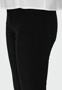 Jeans de mezclilla negra con un diseño ajustado, cintura de media altura y un detalle minimalista en el bolsillo trasero. La tela tiene una textura suave.