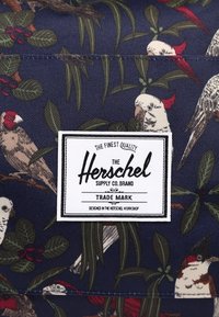 Tkaninowy plecak w kolorze granatowym z wzorem ptaków i liści, z prostokątną biał�ą metką z czarnym napisem "Herschel Supply Co. Brand."