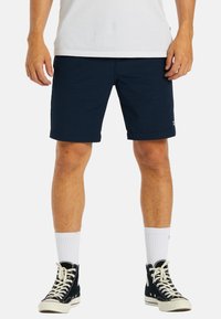 Navy blue, cotton shorts with a straight cut, foldable hem, and side pockets. Paired with black high-top sneakers and white socks.