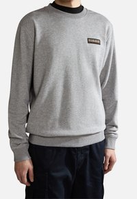 Sweat-shirt gris en tissu doux, avec col rond, poignets et ourlet côtelés, orné d'un petit patch logo sur la poitrine gauche.