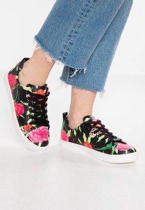 Fødder iført sorte lave sneakers med lyserøde og røde blomsterprint, kombineret med slidte blå jeans.