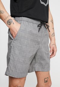 Shorts gris à motif avec une coupe décontractée, dotés d'une taille élastique, d'un cordon de serrage et de poches latérales. Le design à carreaux carrés rehausse la texture.
