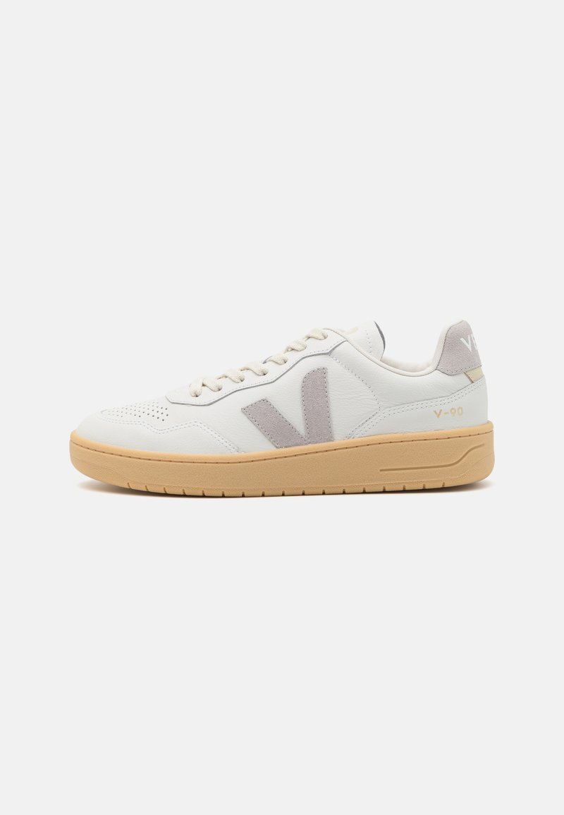 Hvit lær sneaker med grå semsket skinnakenter, snøring, perforert tå og beige gummisåle. Har merkevare på hælen.