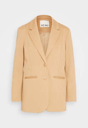 Beige dameblazer med to knapper, hakkede revers og påsatte lommer, vist på en ensfarvet hvid baggrund.