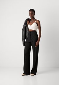 Schwarze weite Hose kombiniert mit einem beigefarbenen strukturierten Croptop und einer schwarzen Lederjacke. Enthält gestapelte silberne Halsketten und beigefarbene Ballerinas.