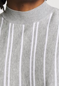 Pull en tricot gris clair avec un col montant côtelé, présentant des rayures blanches verticales et une texture douce.