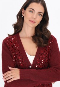 Cardigan tricotat bordeaux cu accente din paiete pe față, decolteu în V și închidere cu un singur buton. Țesătură texturată cu mâneci lungi.