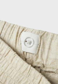Jasno beżowy materiał o teksturowanej, żebrowanej powierzchni i białym zapięciu na guzik. Materiał wydaje się miękki i lekko pomarszczony.